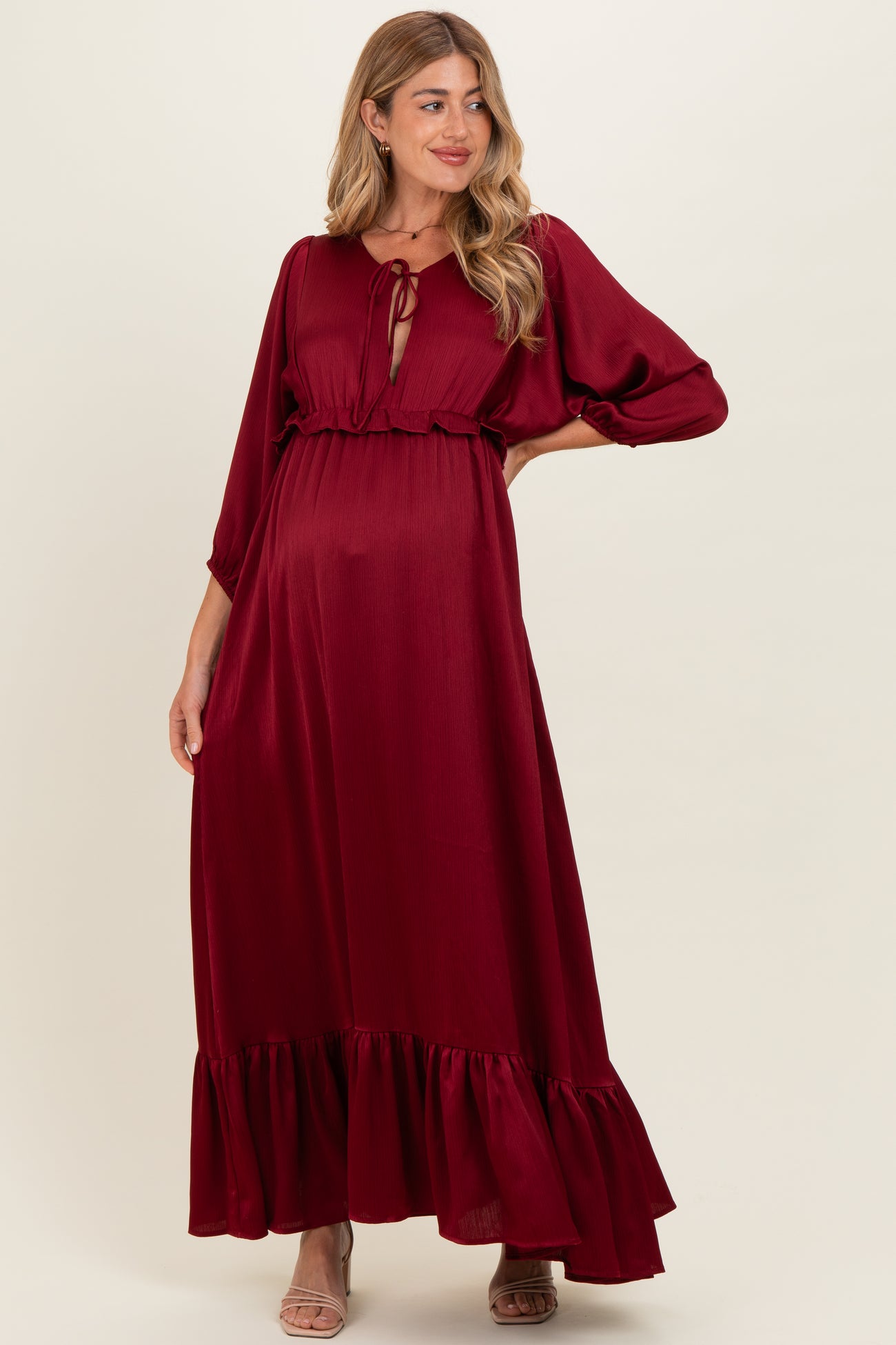 woman wearing a burgundy maternity maxi dress with a tie front and ruffle hem, showing her baby bump