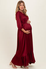 woman wearing a burgundy maternity maxi dress with long sleeves, holding her baby bump