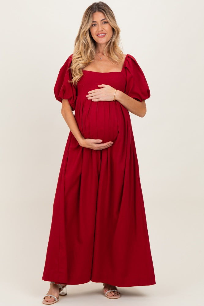 woman wearing a red maternity maxi dress with puff sleeves and holding her baby bump