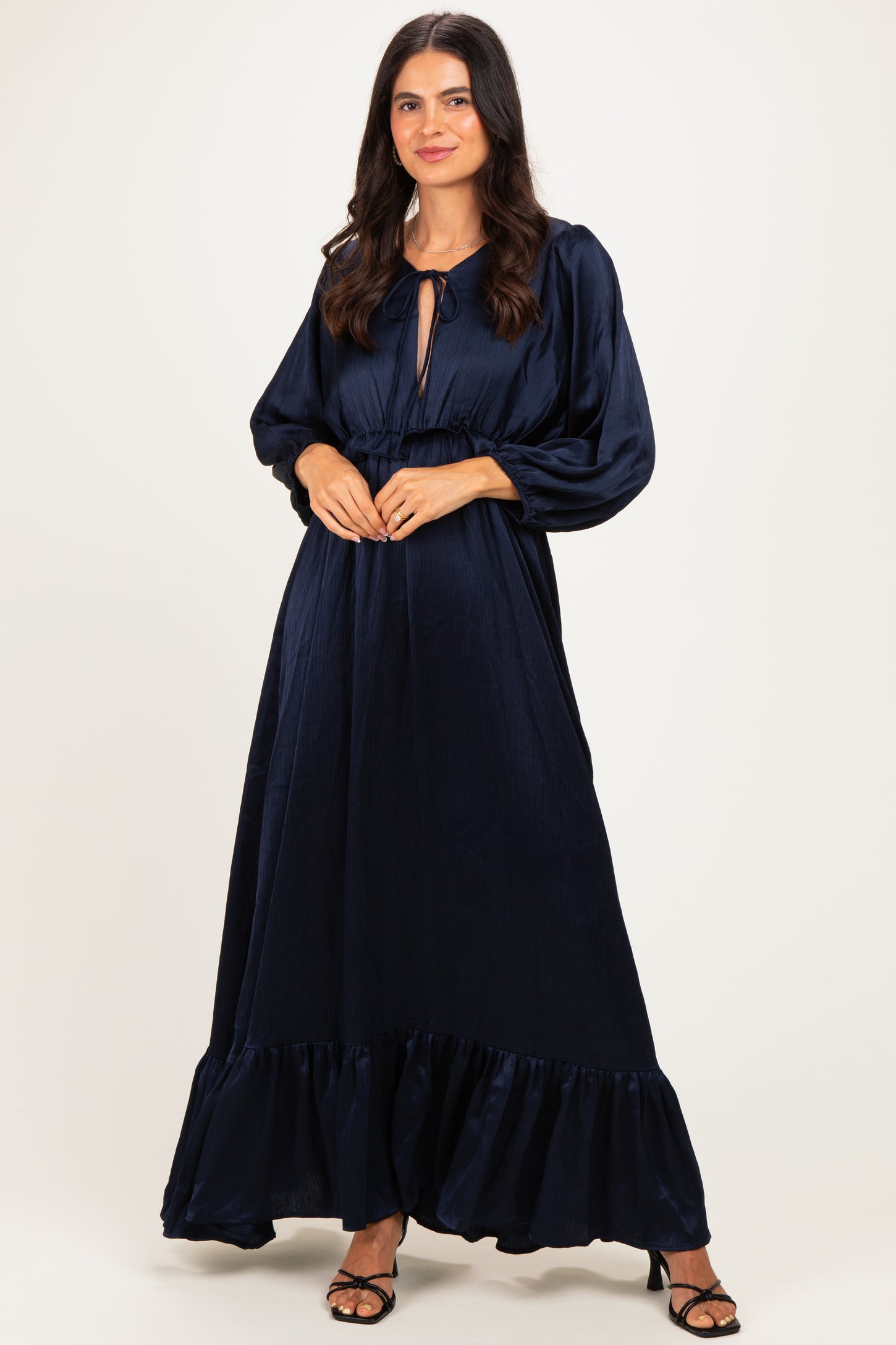 woman wearing a navy blue long sleeve maxi dress with a tie neckline and ruffled hem