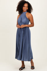 woman wearing a pleated steel blue maxi dress with a halter neck and a fitted waist, posing with one hand on her hip