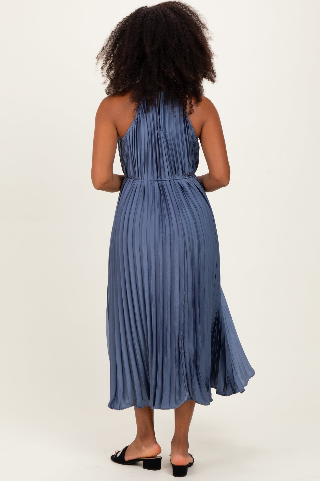 woman wearing a pleated blue midi dress with a halter neckline and open back, viewed from the back