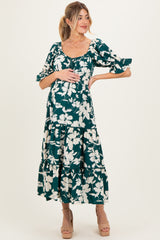 woman wearing a dark green floral print maternity dress with tiered ruffles and a baby bump visible