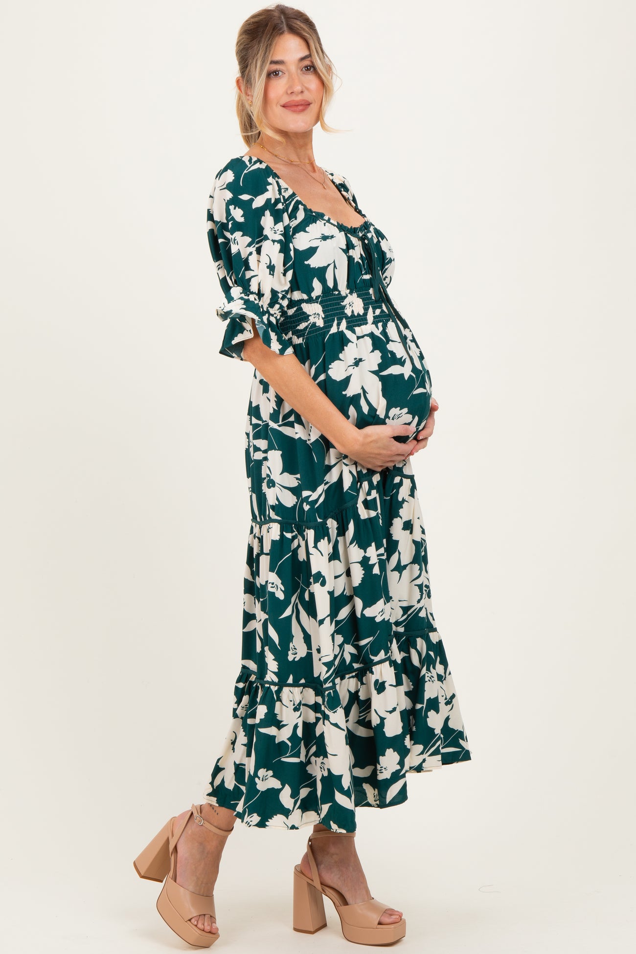 woman wearing a green floral maternity maxi dress, highlighting her baby bump while standing in side profile