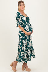 woman wearing a green floral maternity maxi dress, highlighting her baby bump while standing in side profile