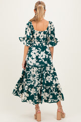 woman wearing a dark green floral print maternity dress with puff sleeves and a tiered skirt