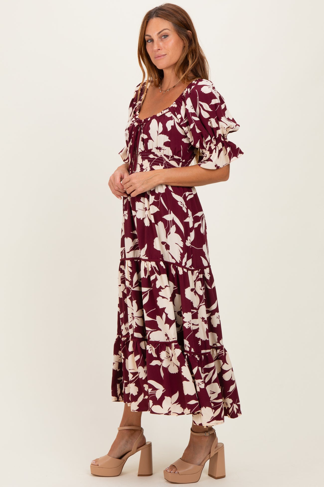 woman wearing a burgundy floral maxi dress with ruffle sleeves and tiered hem, paired with beige platform heels