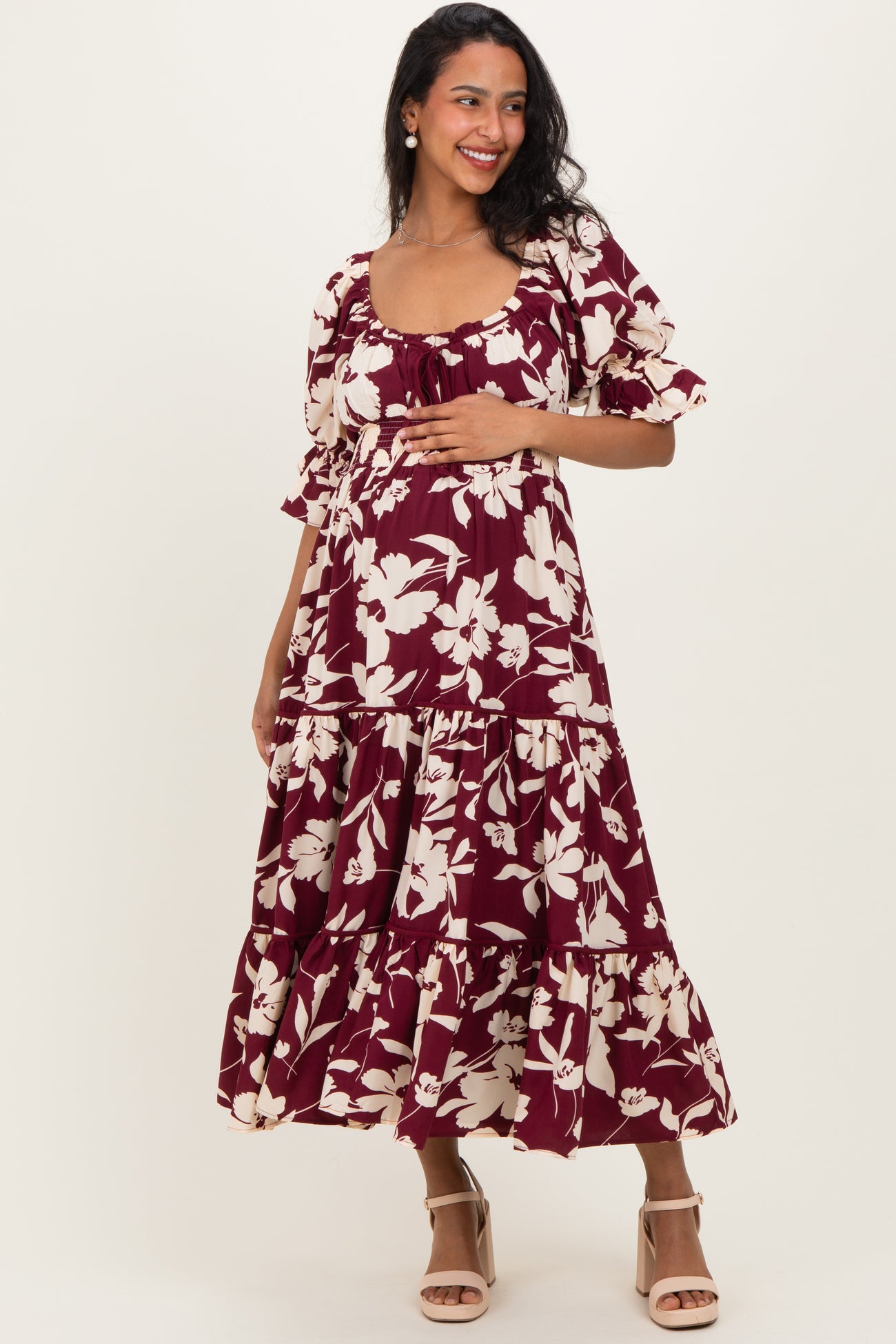 woman wearing a burgundy maternity dress with floral print and ruffled tiers, holding her baby bump