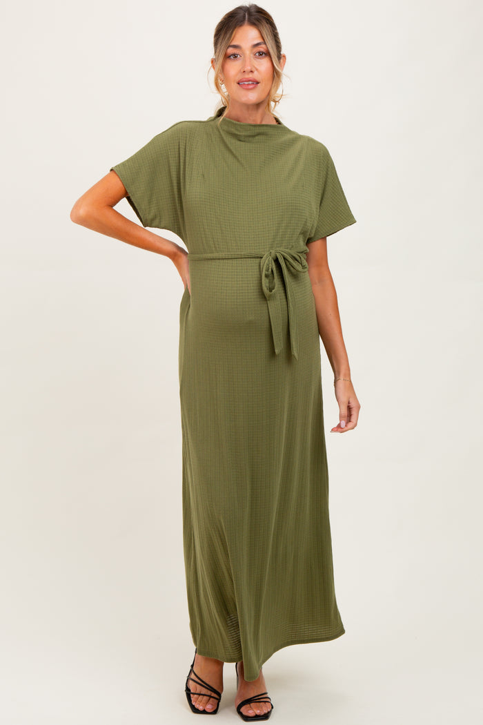 woman wearing an olive green maternity maxi dress with a tie waist and short sleeves, showing her baby bump