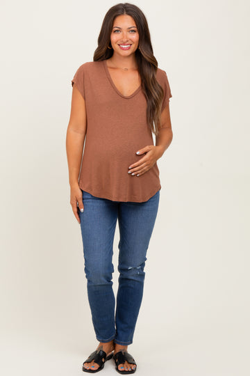 woman wearing a rust v-neck maternity top and blue jeans, holding her baby bump
