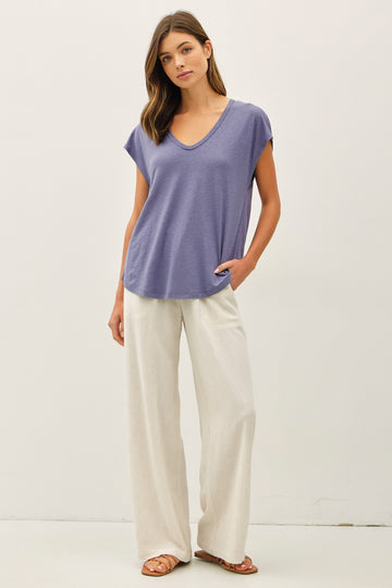 woman wearing a purple short sleeve v-neck top with a front pocket and cream wide-leg pants