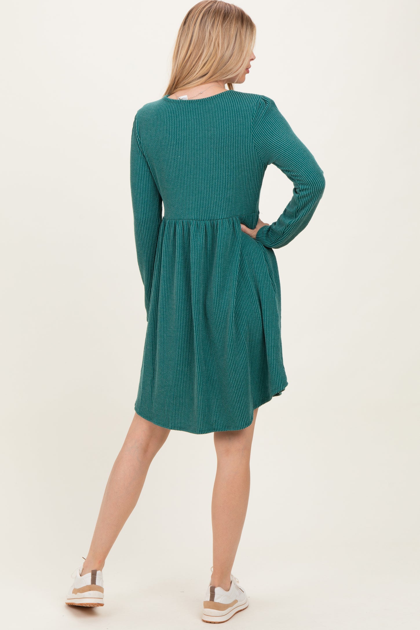 woman wearing a teal ribbed long sleeve dress with a flared skirt and back pleat, paired with white sneakers