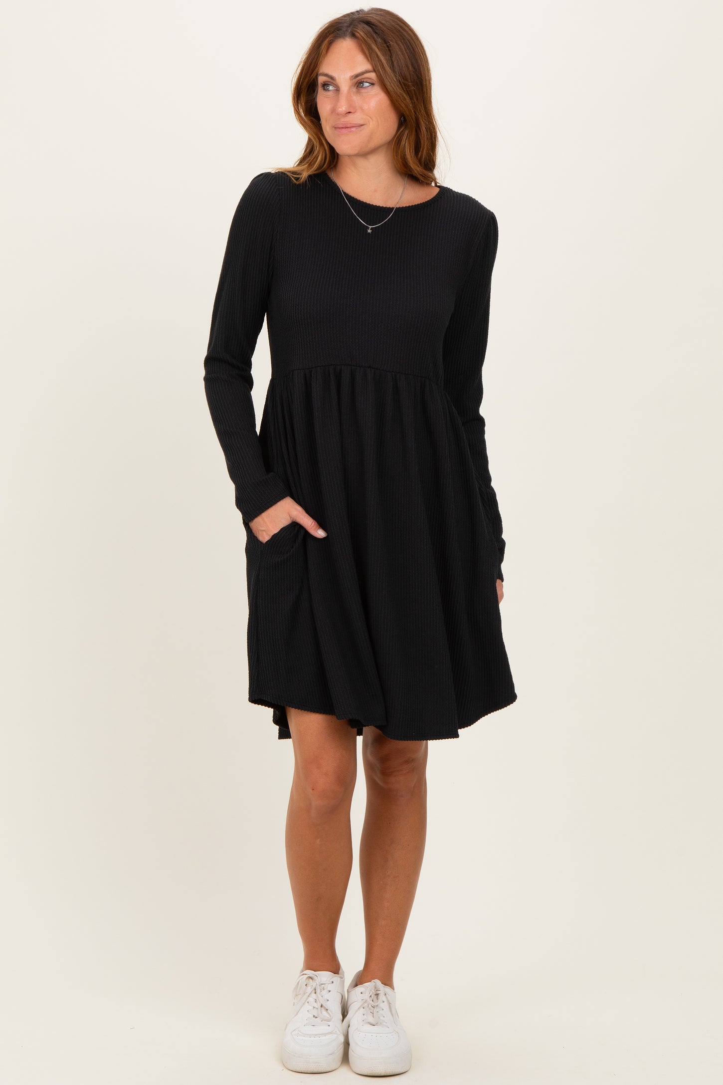 woman wearing a black long sleeve dress with a textured bodice and flared skirt, featuring pockets and paired with white sneakers