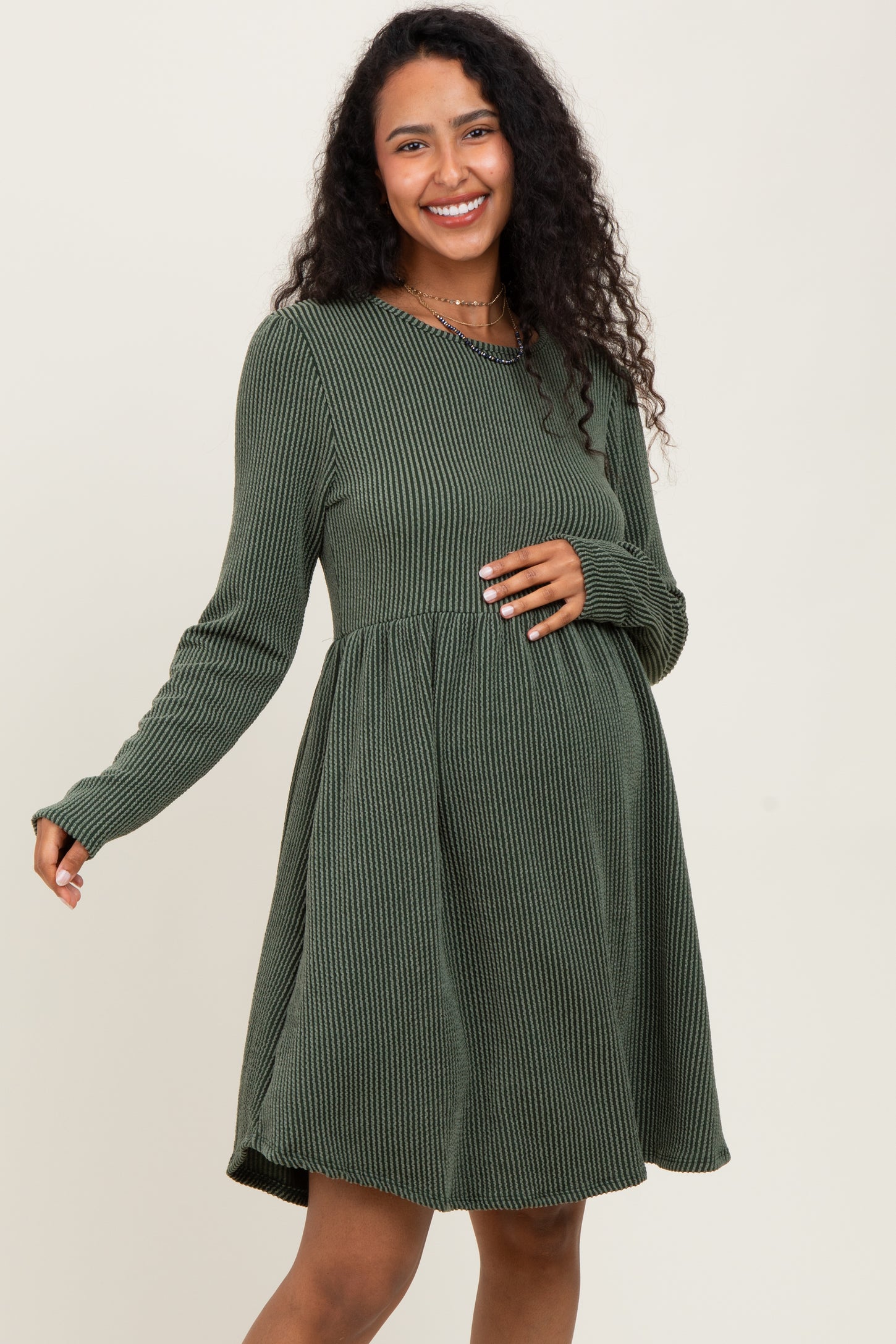 woman wearing a dark green ribbed long sleeve maternity dress with a baby bump visible