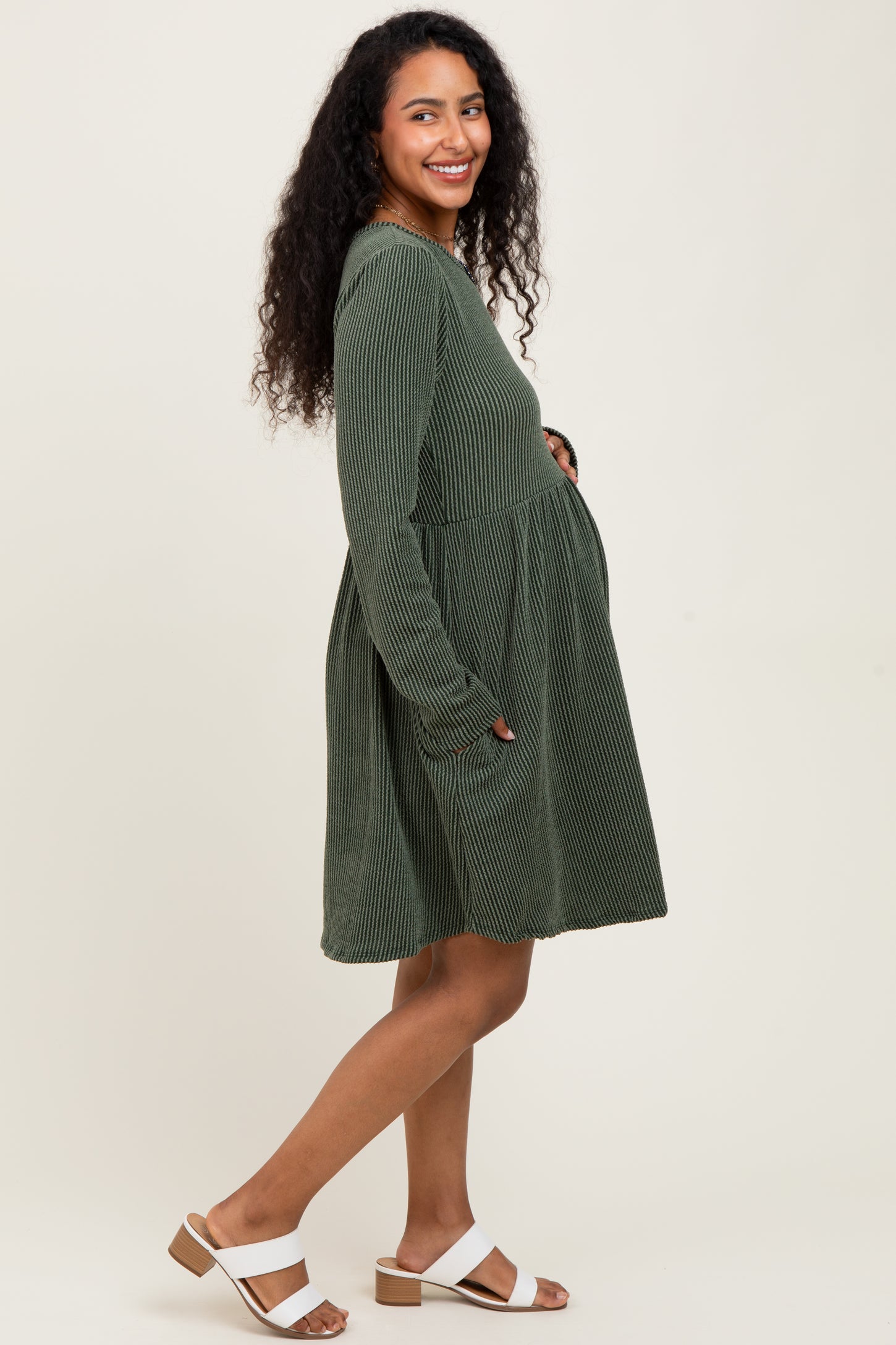 woman wearing a dark green striped maternity dress with long sleeves and pockets, showing her baby bump