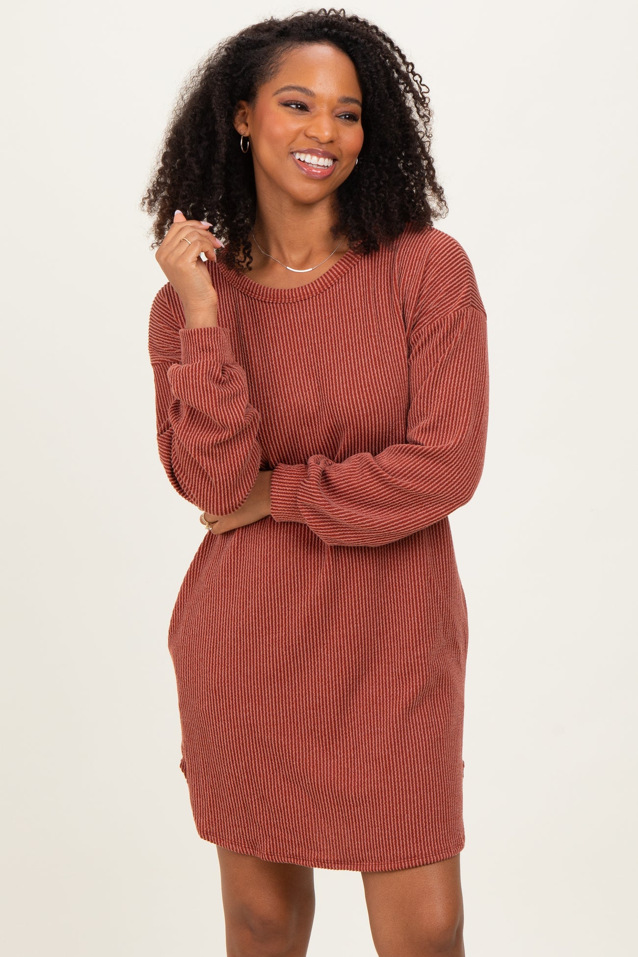 woman wearing a rust-colored ribbed long sleeve dress with a relaxed fit and subtle side slits