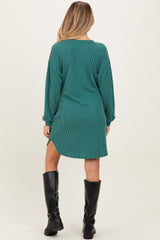 woman wearing a green striped maternity dress with long sleeves and side slits, standing with her back to the camera