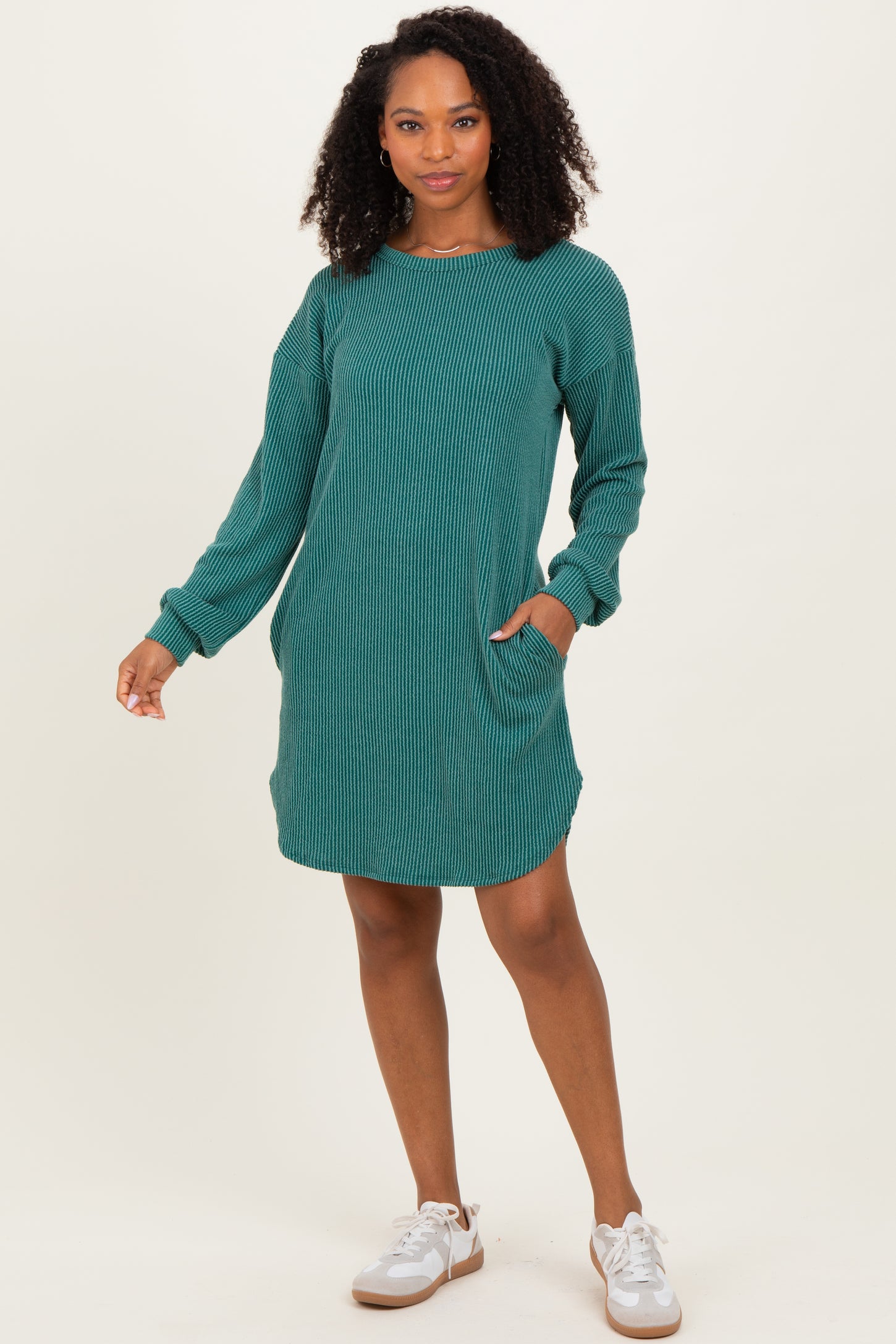 woman wearing a teal ribbed long sleeve dress with pockets and a relaxed fit, smiling and standing against a neutral background