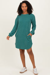woman wearing a teal ribbed long sleeve dress with pockets and a relaxed fit, smiling and standing against a neutral background