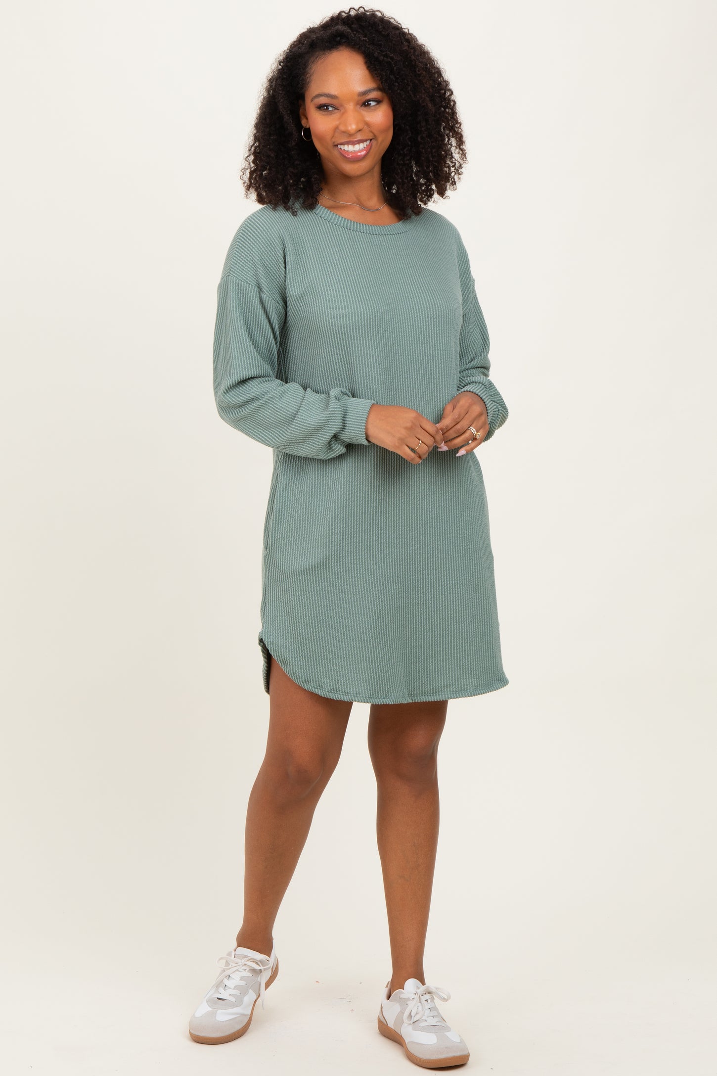 woman wearing a green ribbed long sleeve dress with side slits and a relaxed fit, standing with a smile