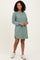 woman wearing a green ribbed long sleeve dress with side slits and a relaxed fit, standing with a smile