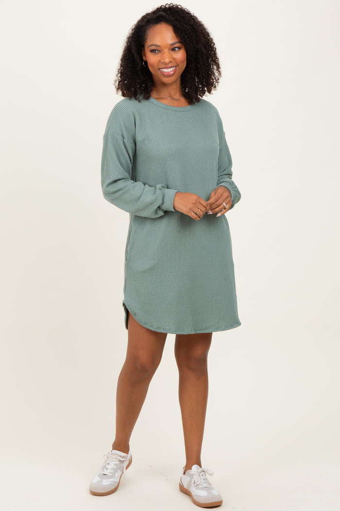 woman wearing a green ribbed long sleeve dress with side slits and a relaxed fit, standing with a smile