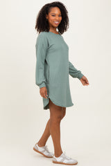 woman wearing a green ribbed long sleeve sweater dress, standing sideways, showing a relaxed fit and a high-low hemline