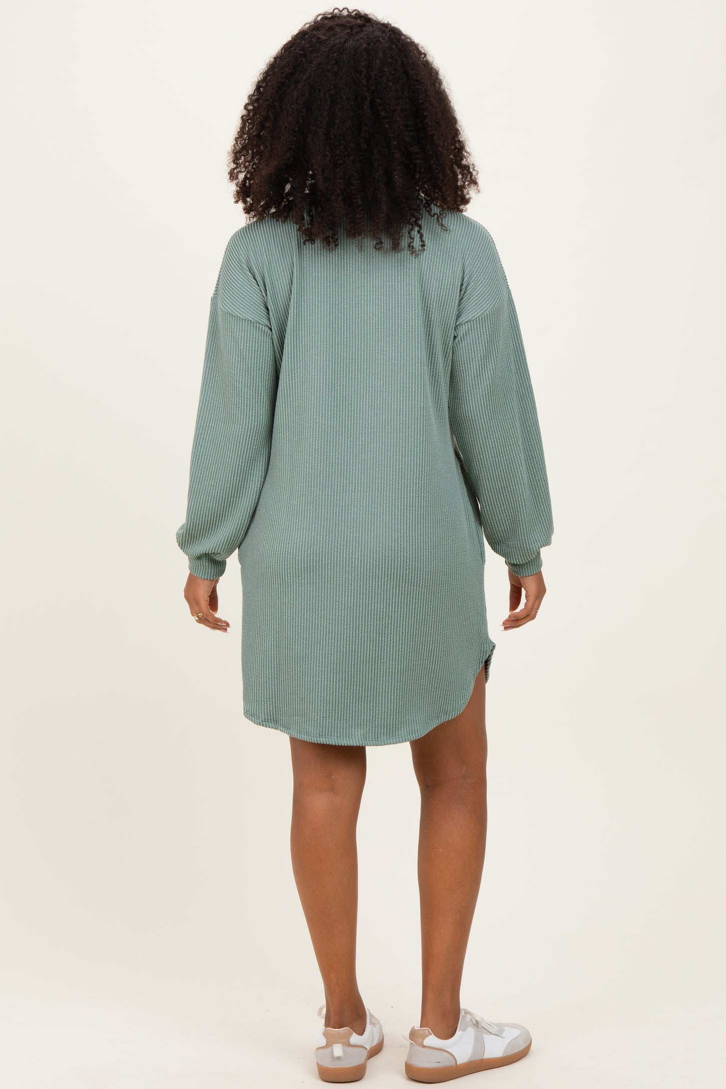 woman wearing a green ribbed long sleeve oversized dress with a high-low hem and white sandals