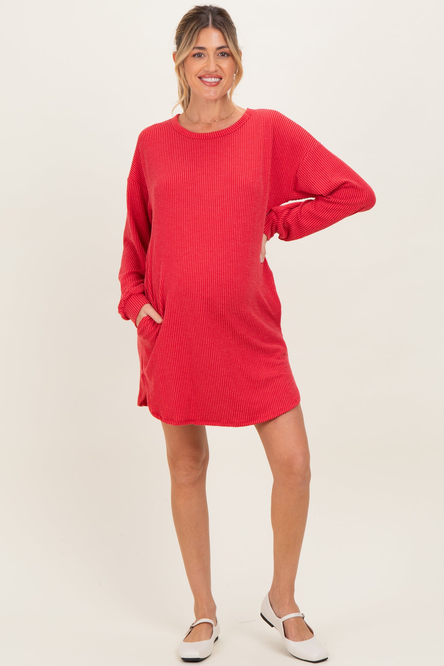woman wearing a red ribbed maternity dress with long sleeves and pockets, featuring a visible baby bump