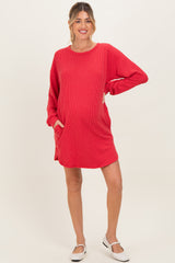 woman wearing a red ribbed maternity dress with long sleeves and pockets, featuring a visible baby bump