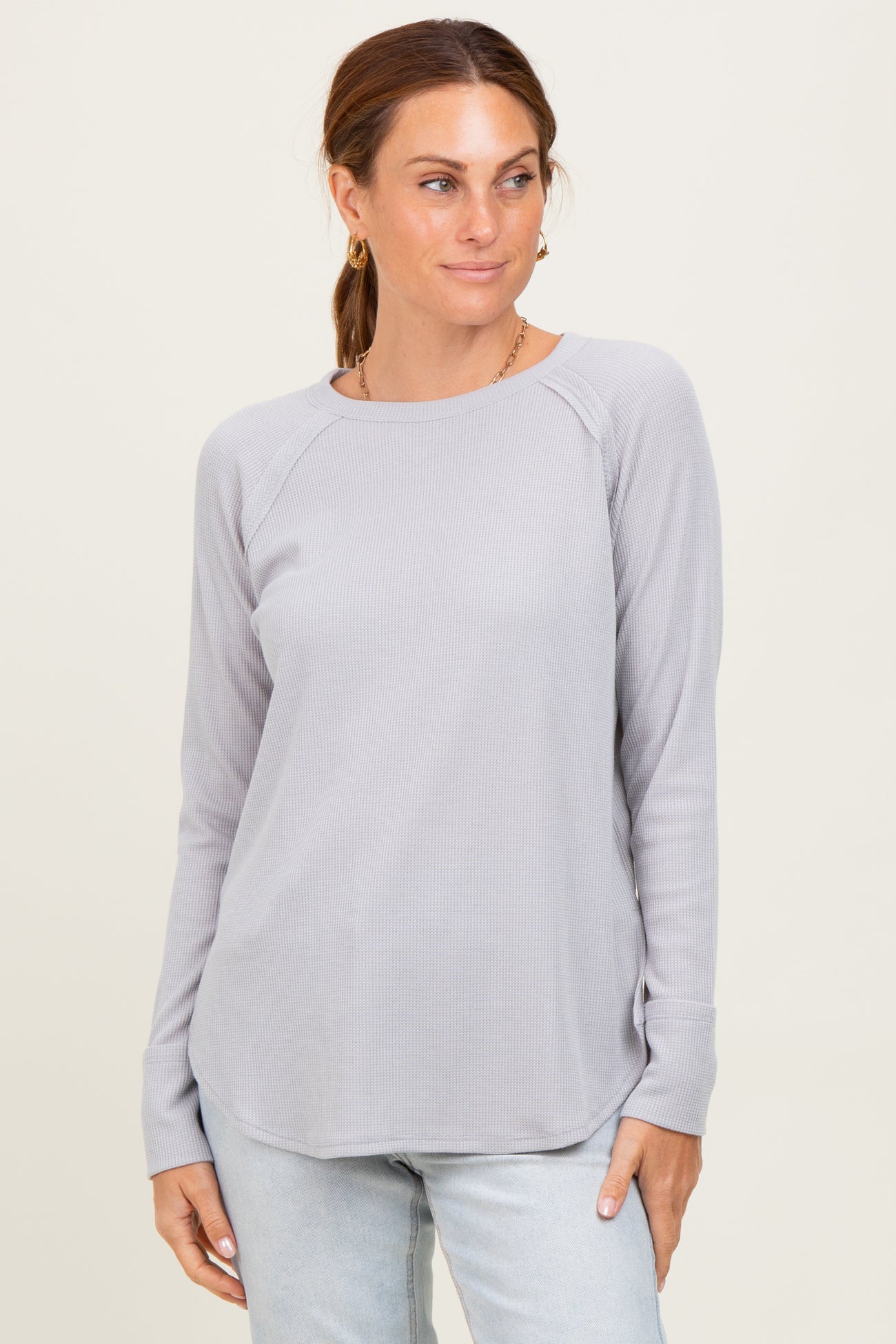 woman wearing a light gray long sleeve ribbed top with raglan sleeves and a rounded hem