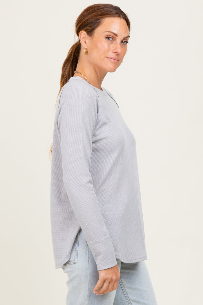 woman wearing a light gray long sleeve ribbed top with side slits and relaxed fit, paired with light blue jeans