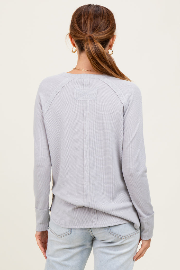 woman wearing a light grey long sleeve ribbed top, showing a back view with a stitched detail