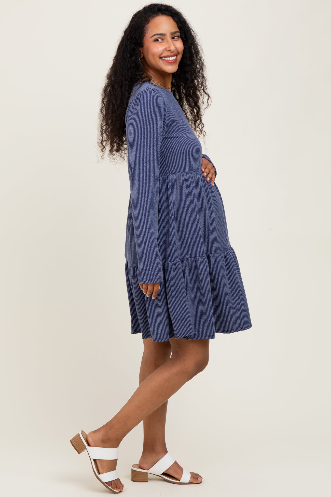 woman wearing a navy blue striped long sleeve maternity dress with a tiered skirt and holding her baby bump