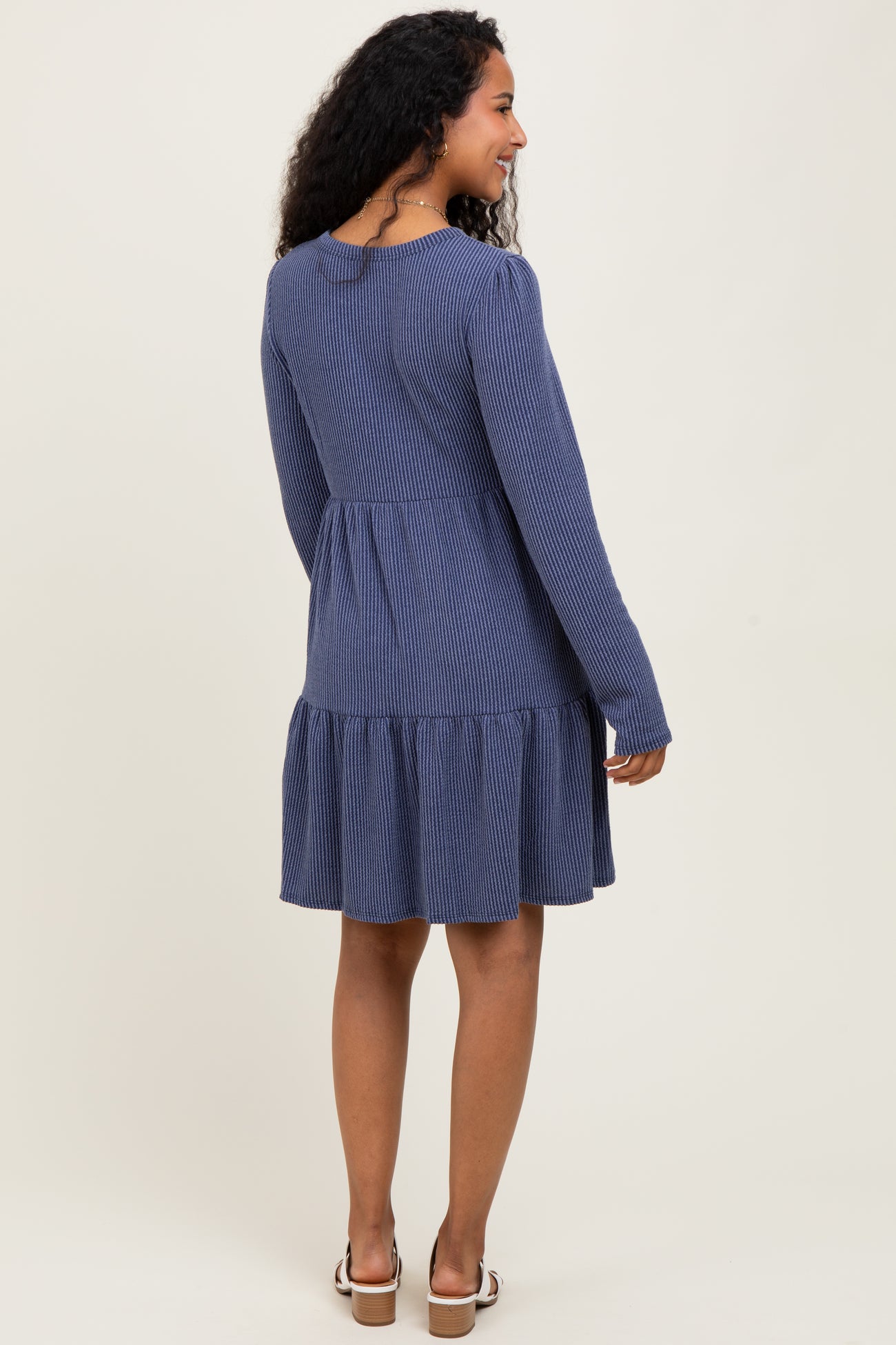 woman wearing a navy blue striped long sleeve maternity dress with a ruffled hem, looking back at the camera