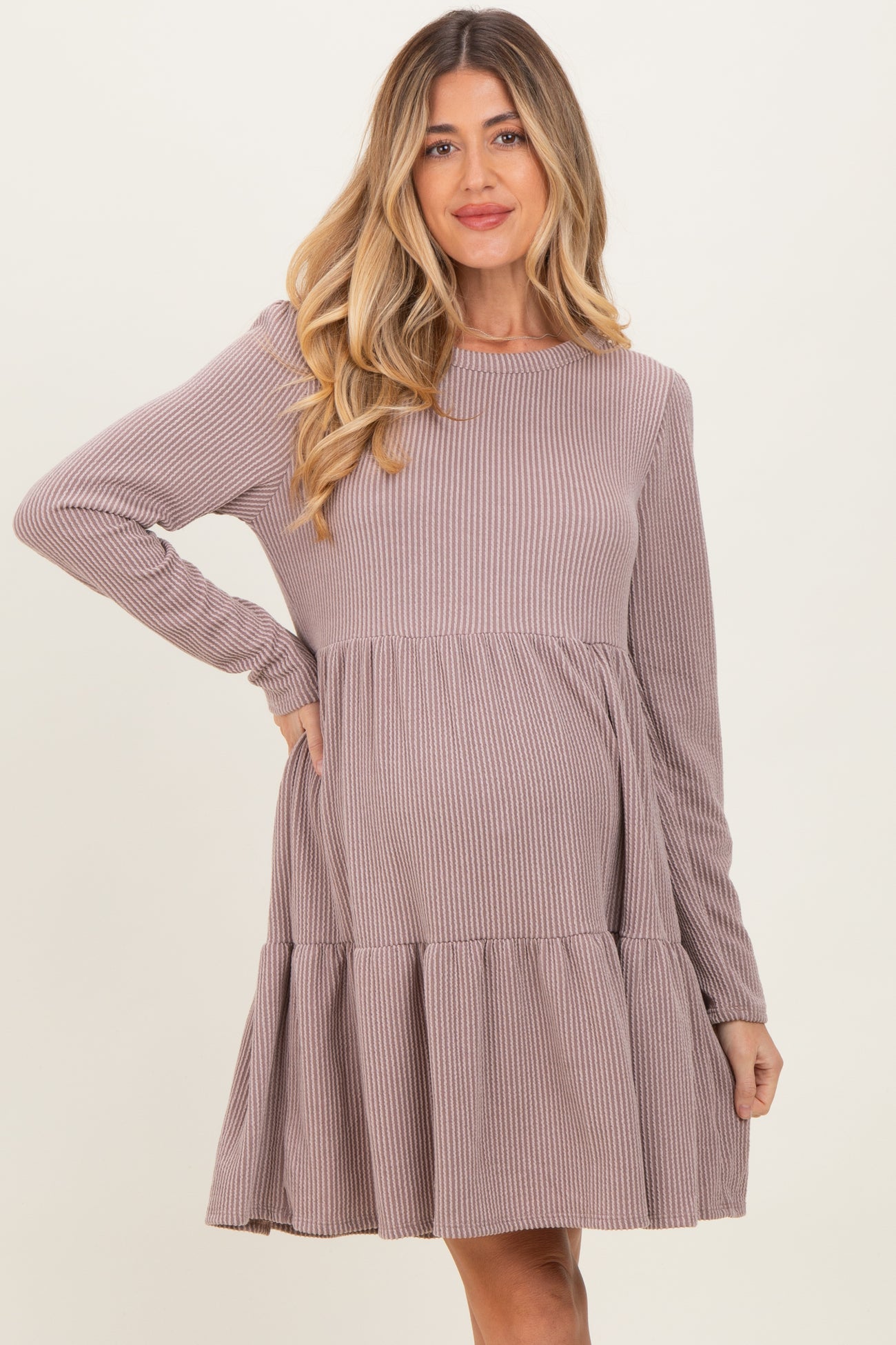 woman wearing a mauve ribbed maternity dress with long sleeves and a tiered skirt, showcasing her baby bump