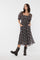 woman wearing a black floral midi dress with puff sleeves and pockets, paired with black ankle boots