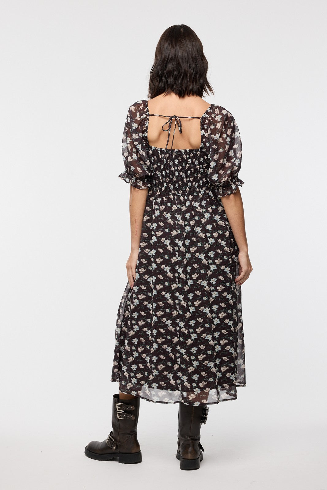 woman wearing a black floral maxi dress with puff sleeves and back tie detail, paired with knee-high boots