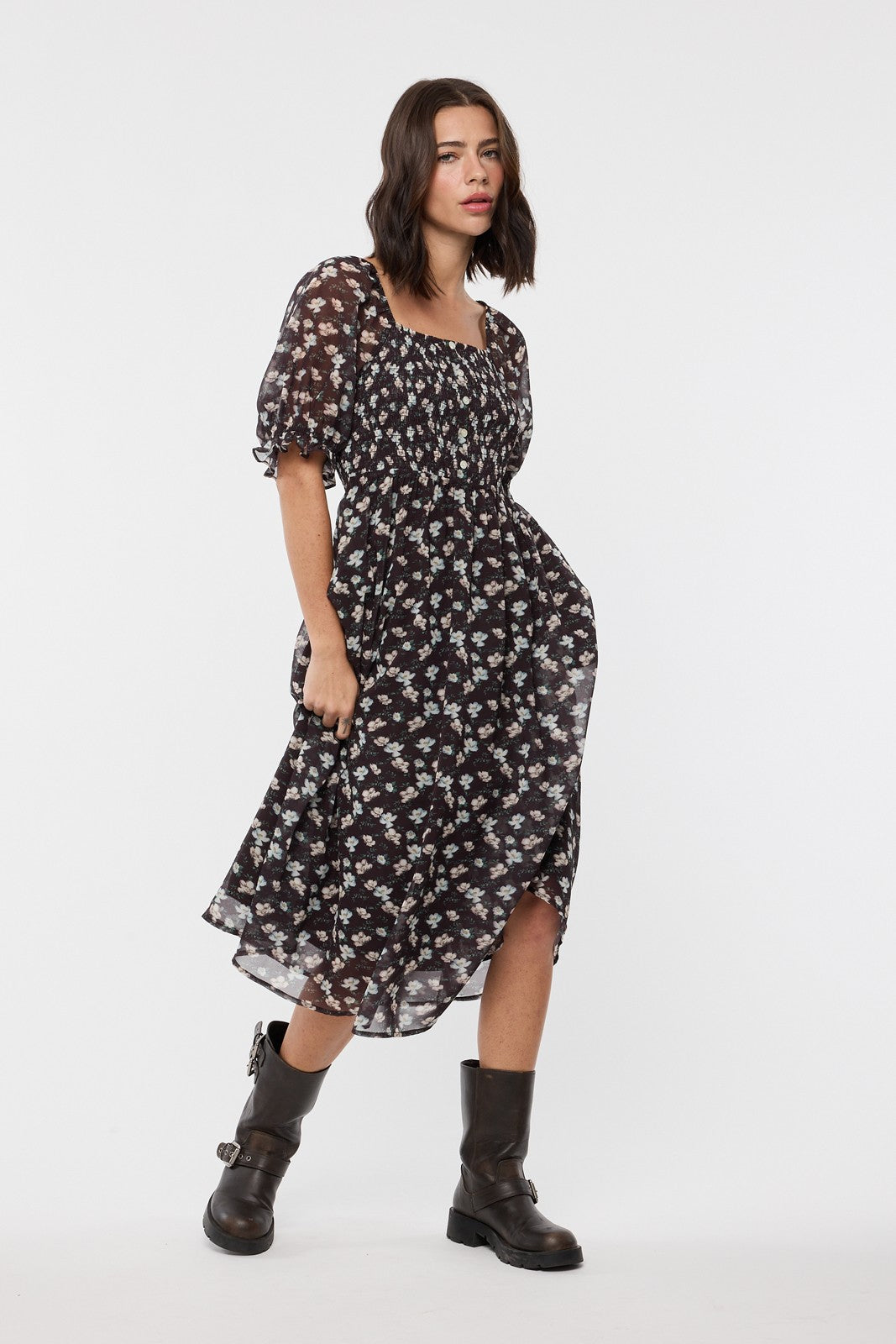 woman wearing a black floral midi dress with puffed sleeves and a smocked bodice, paired with black ankle boots