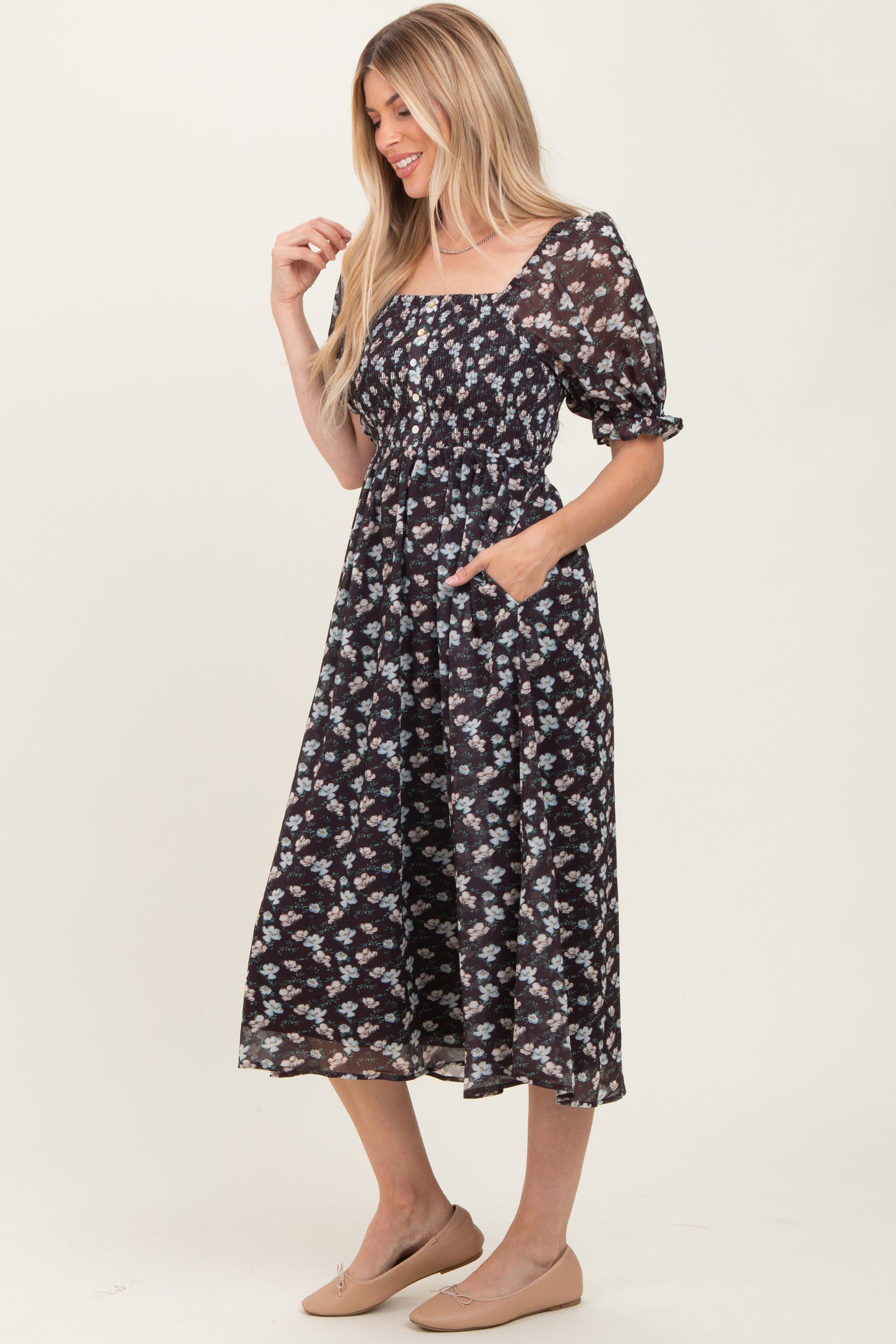 woman wearing a black floral midi dress with puff sleeves and a square neckline, featuring a fitted bodice and side pockets