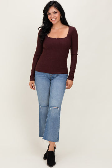 woman wearing a maroon ribbed long sleeve top with a square neckline and distressed light blue flared jeans