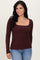 woman wearing a burgundy long sleeve ribbed top with a scoop neckline and a bow detail