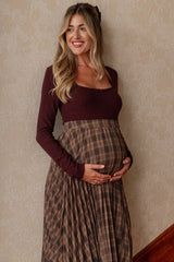 woman wearing a burgundy long sleeve maternity top and a brown plaid maternity skirt, showing her baby bump