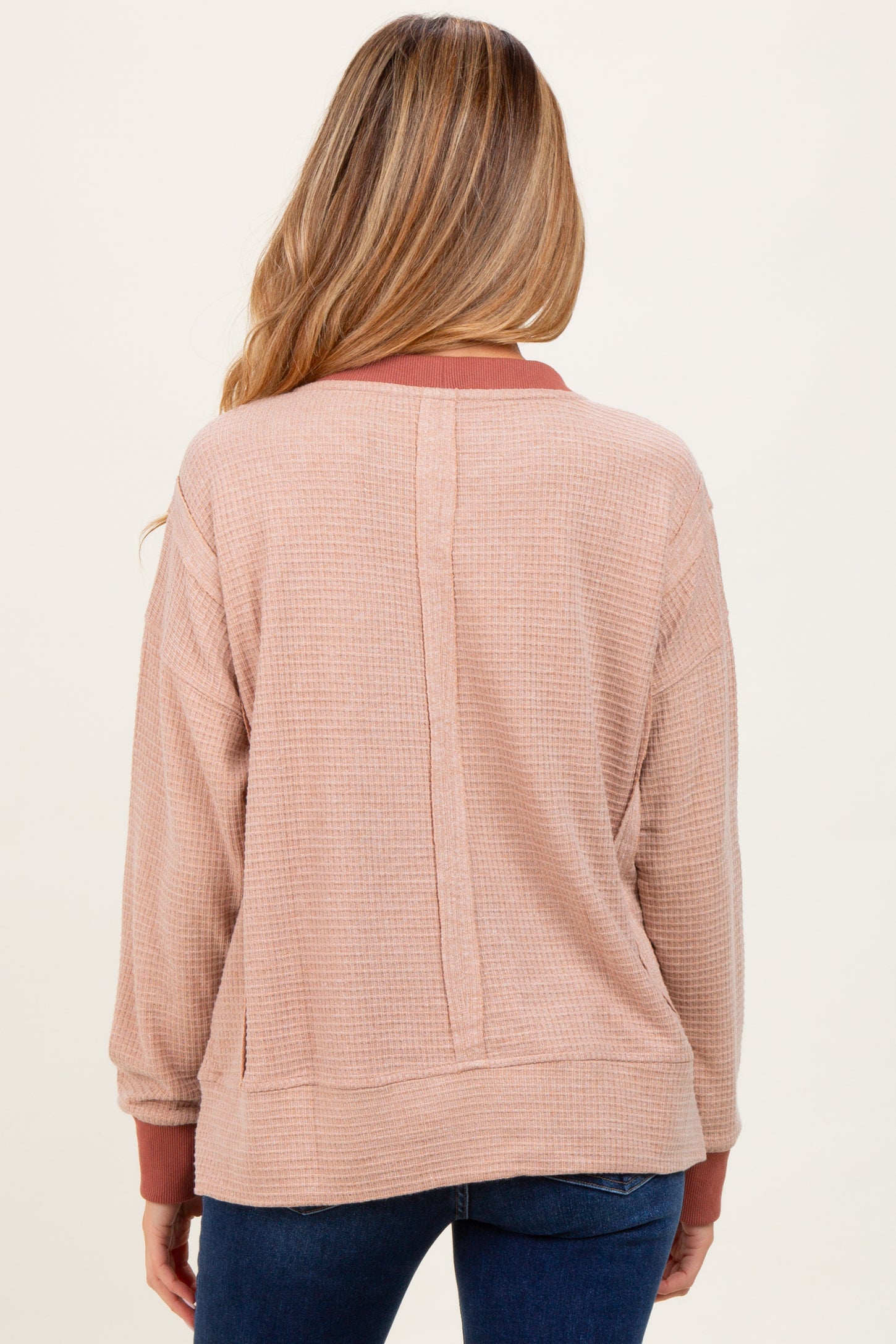 woman wearing a light pink maternity pullover with a slightly textured fabric and contrasting burgundy collar, seen from the back