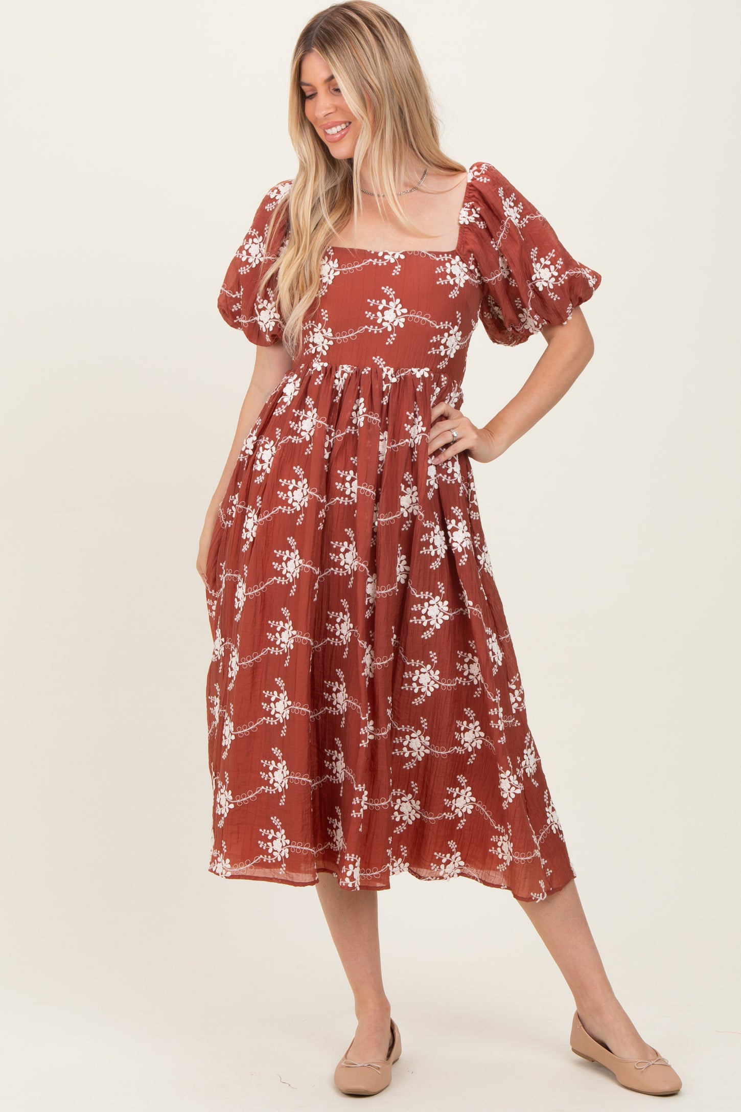 woman wearing a rust-colored midi dress with puff sleeves and a floral pattern