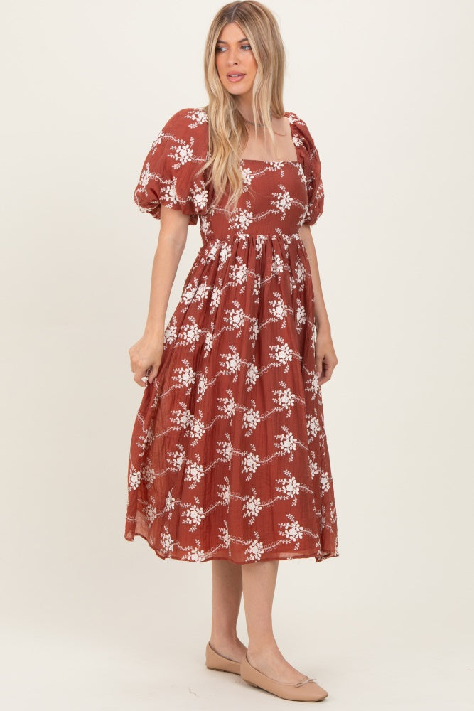 woman wearing a rust colored midi dress with puff sleeves and floral print, standing in profile