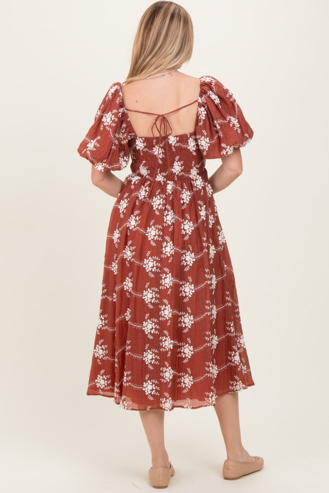 woman wearing a rust-colored floral print midi dress with puff sleeves and a smocked back detail
