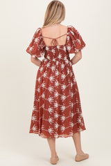 woman wearing a rust-colored floral print midi dress with puff sleeves and a smocked back detail