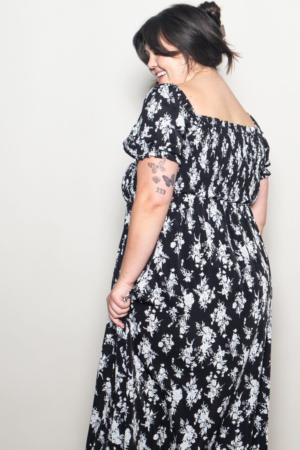 woman wearing a black floral print plus-size maxi dress with short puff sleeves and a square neckline, smiling