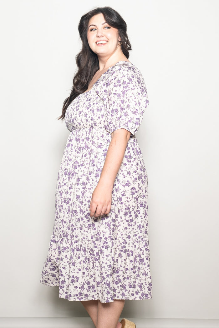 plus size woman wearing a purple floral midi dress with short sleeves and a cinched waist